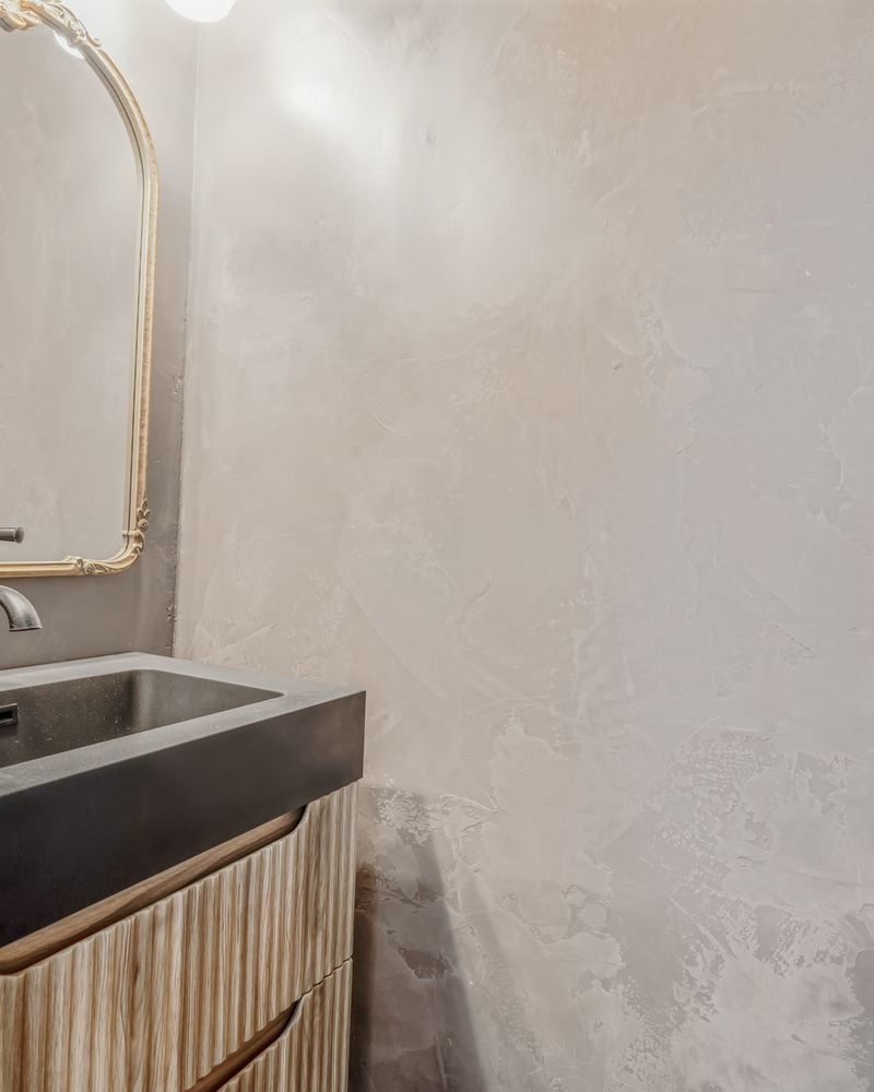 Powder room with concrete vessel sink and brass mirror